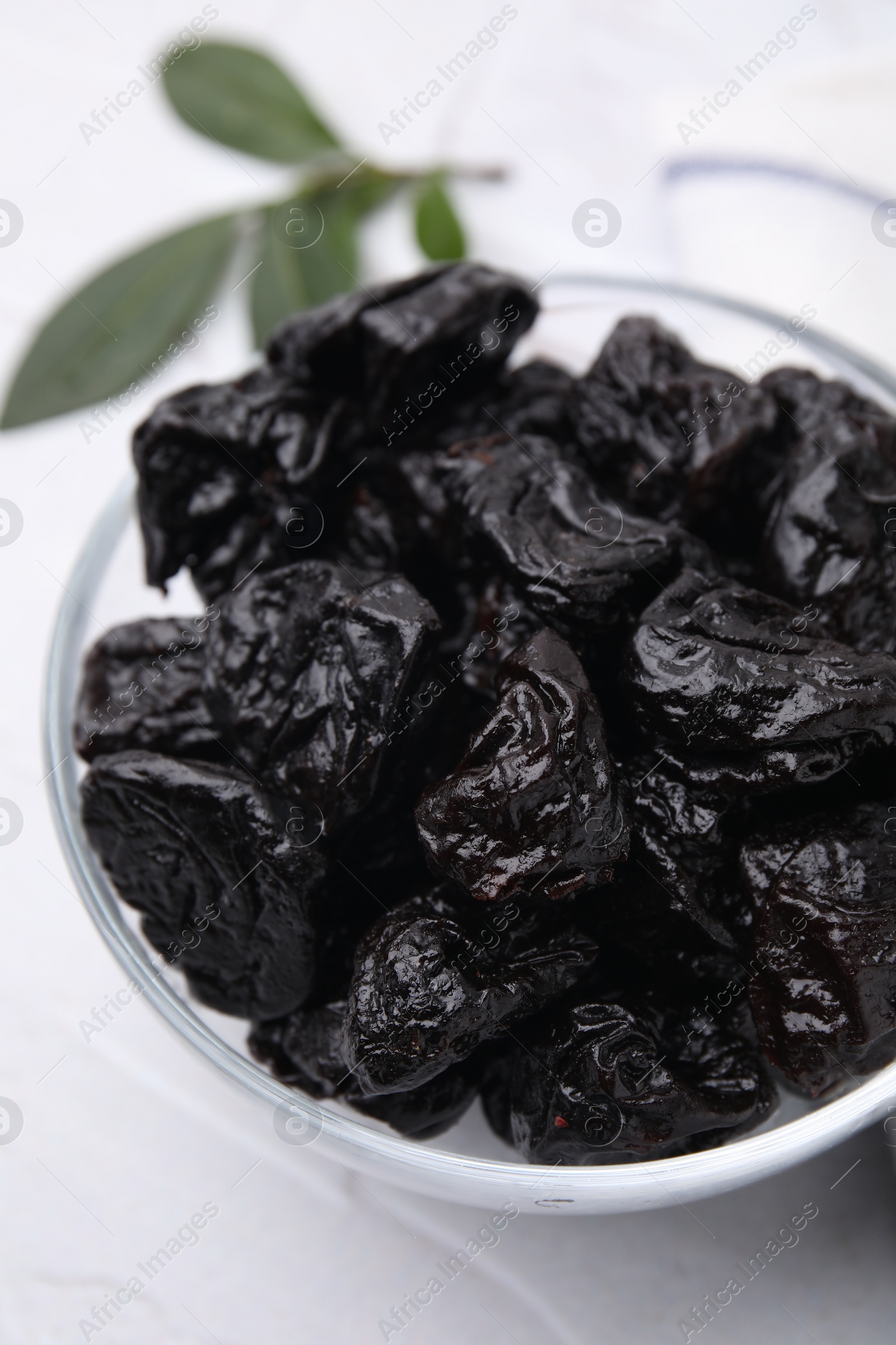 Photo of Sweet dried prunes in bowl on white table, closeup