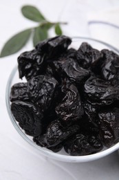 Photo of Sweet dried prunes in bowl on white table, closeup