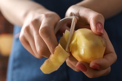 Woman peeling fresh potato indoors, closeup view