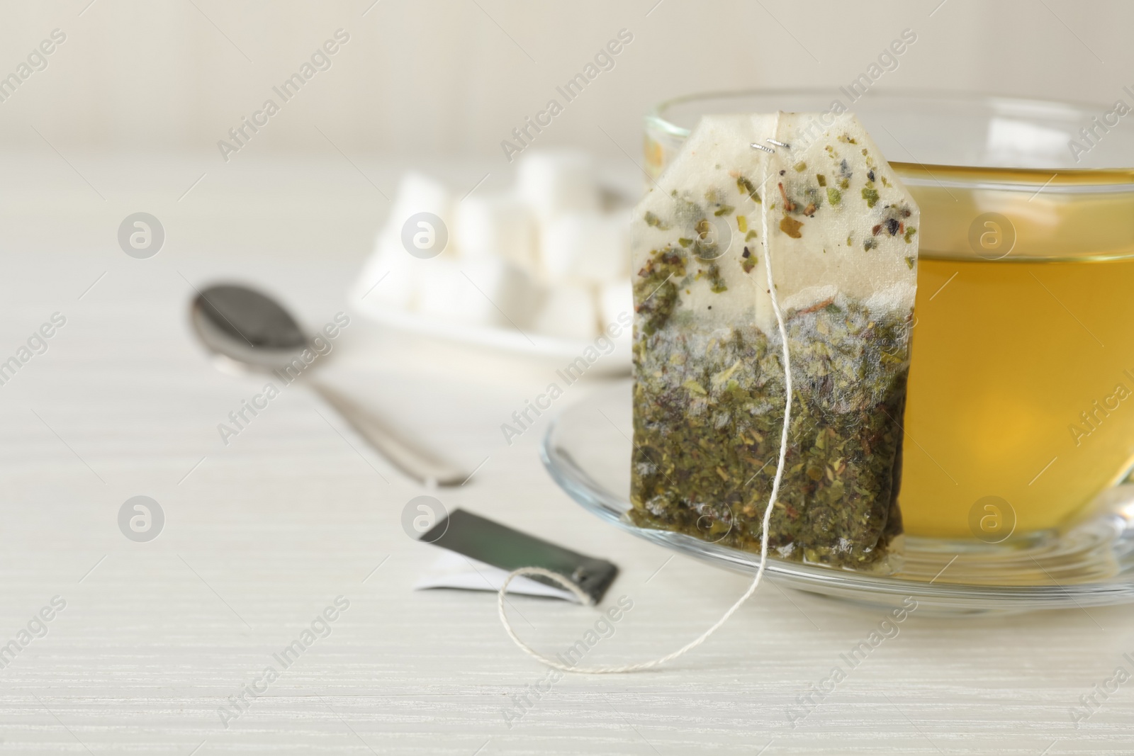 Photo of Used tea bag and cup of hot drink on white wooden table, closeup. Space for text