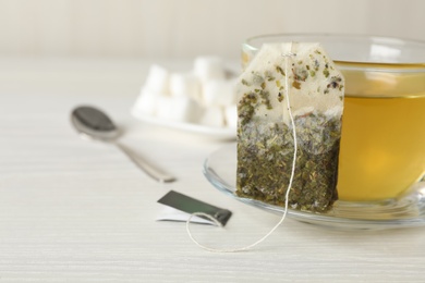 Used tea bag and cup of hot drink on white wooden table, closeup. Space for text