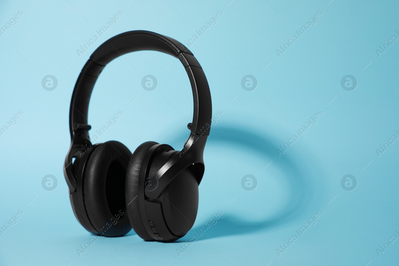 Photo of Modern wireless headphones on light blue background. Space for text