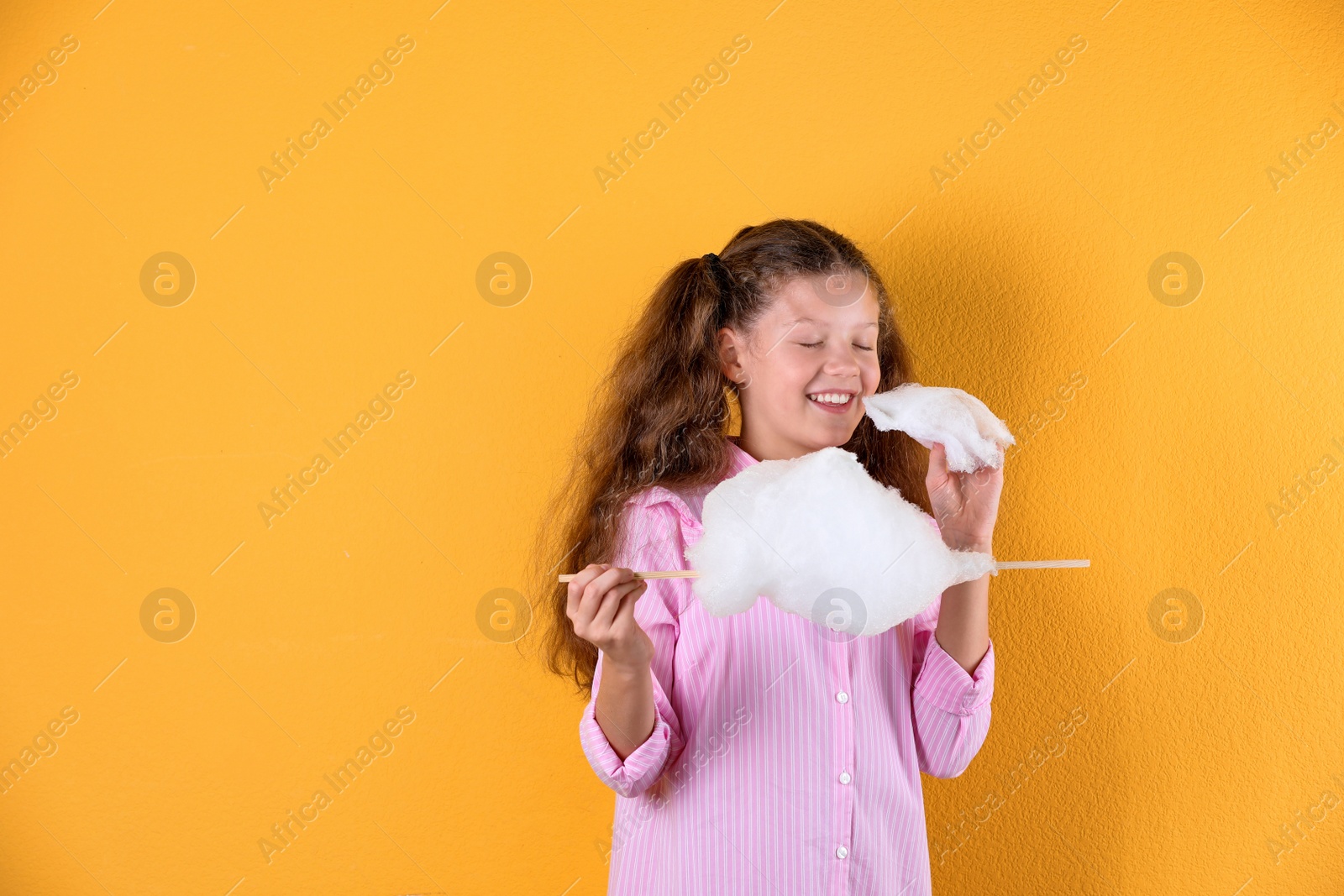 Photo of Little girl with cotton candy on color background