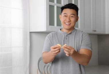 Photo of Happy asian man holding tasty fortune cookie with prediction indoors