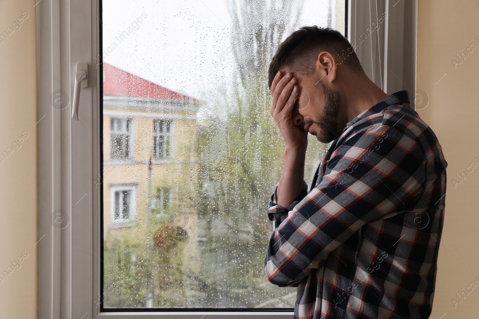 Photo of Depressed man near window at home. Space for text