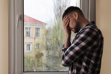 Depressed man near window at home. Space for text