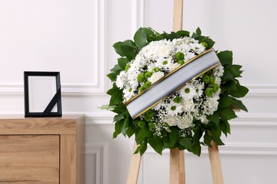 Photo of Wreath of flowers and photo frame with black ribbon on commode in room. Funeral attributes