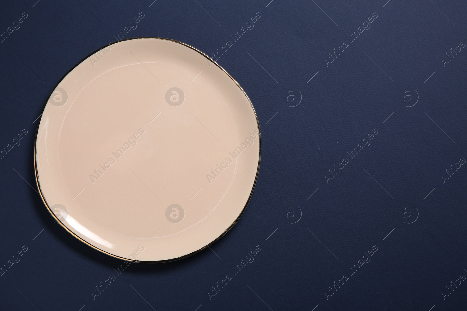 Photo of One beige ceramic plate on dark blue background, top view. Space for text