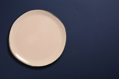 Photo of One beige ceramic plate on dark blue background, top view. Space for text