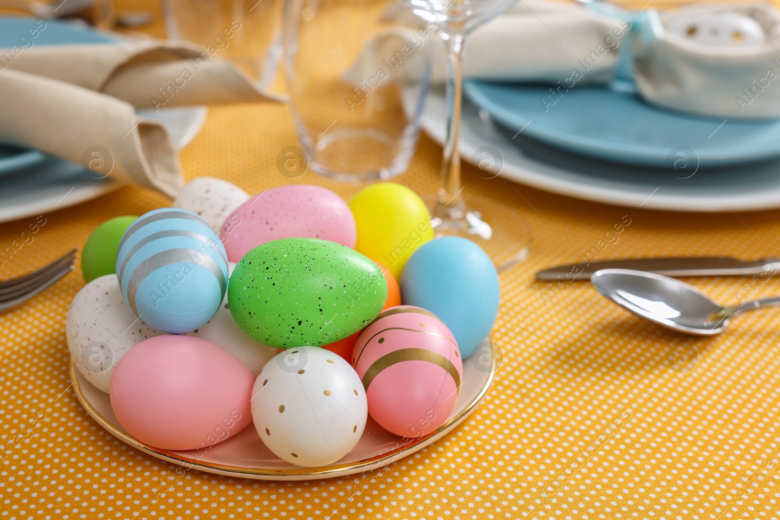 Photo of Festive table setting with painted eggs, glasses and cutlery. Easter celebration