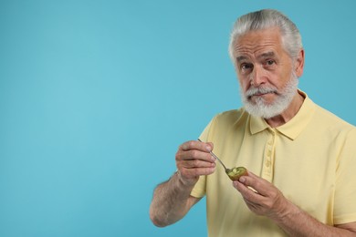 Photo of Senior man eating kiwi with spoon on light blue background, space for text