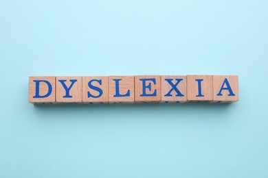 Wooden cubes with word Dyslexia on light blue background, flat lay