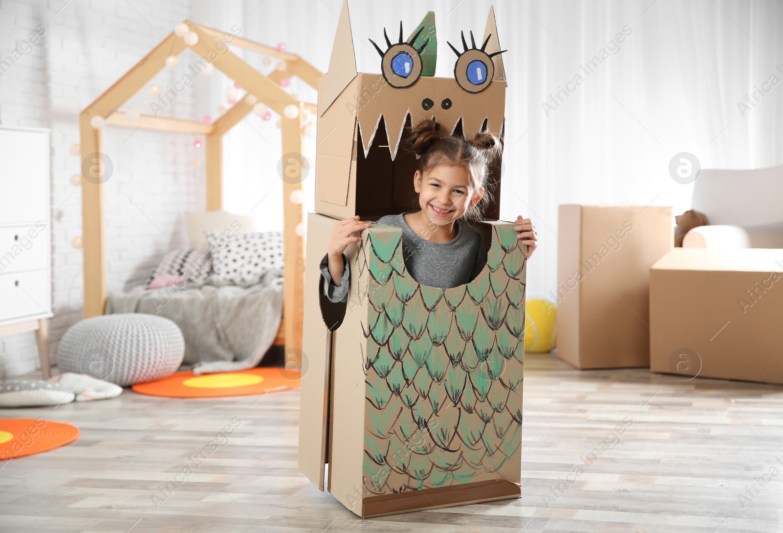 Photo of Cute little girl in cardboard costume of dinosaur at home