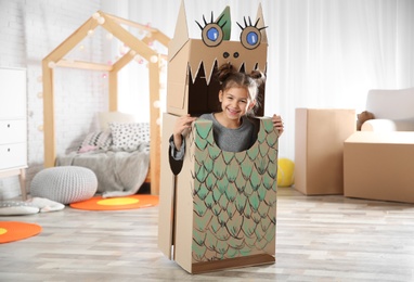Photo of Cute little girl in cardboard costume of dinosaur at home