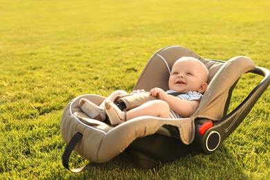 Adorable baby in child safety seat on green grass