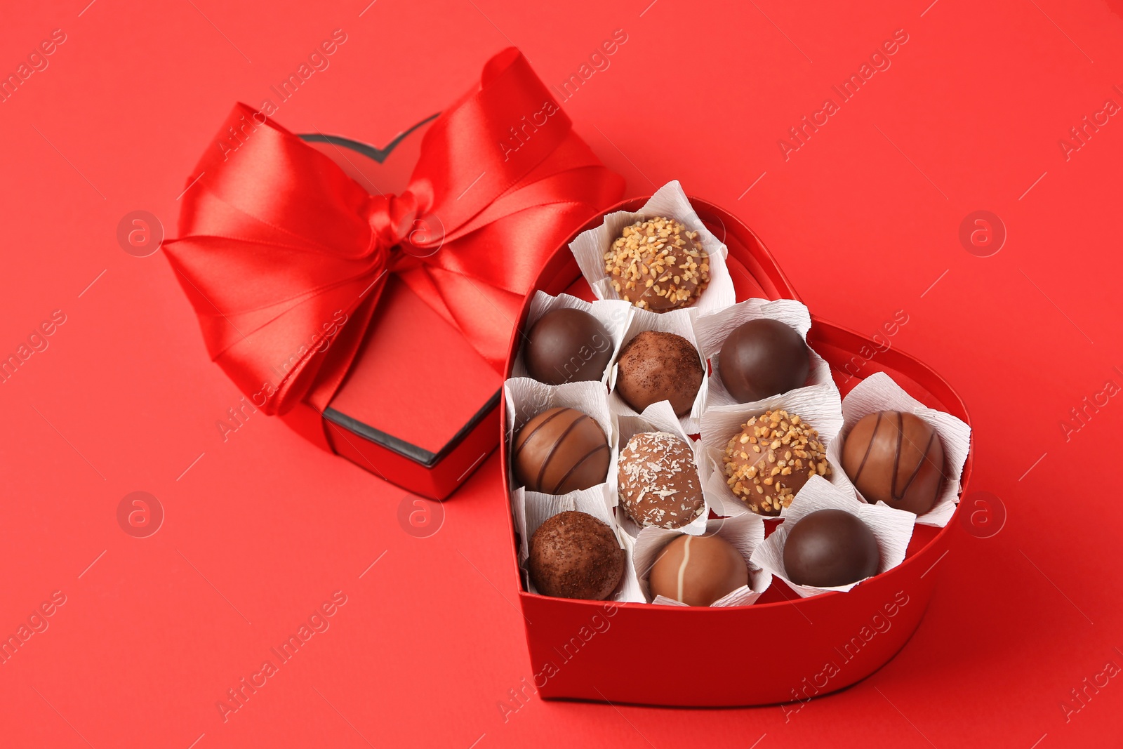 Photo of Heart shaped box with delicious chocolate candies on red table