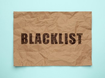Crumpled paper with word Blacklist on light blue background, top view