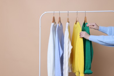 Photo of Woman taking sweater from rack on beige background, closeup. Space for text