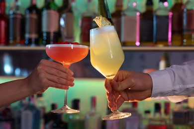 Photo of Man and woman clinking glasses with alcoholic cocktails in bar, closeup