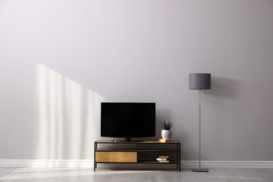 Elegant room interior with TV on cabinet and lamp near light wall