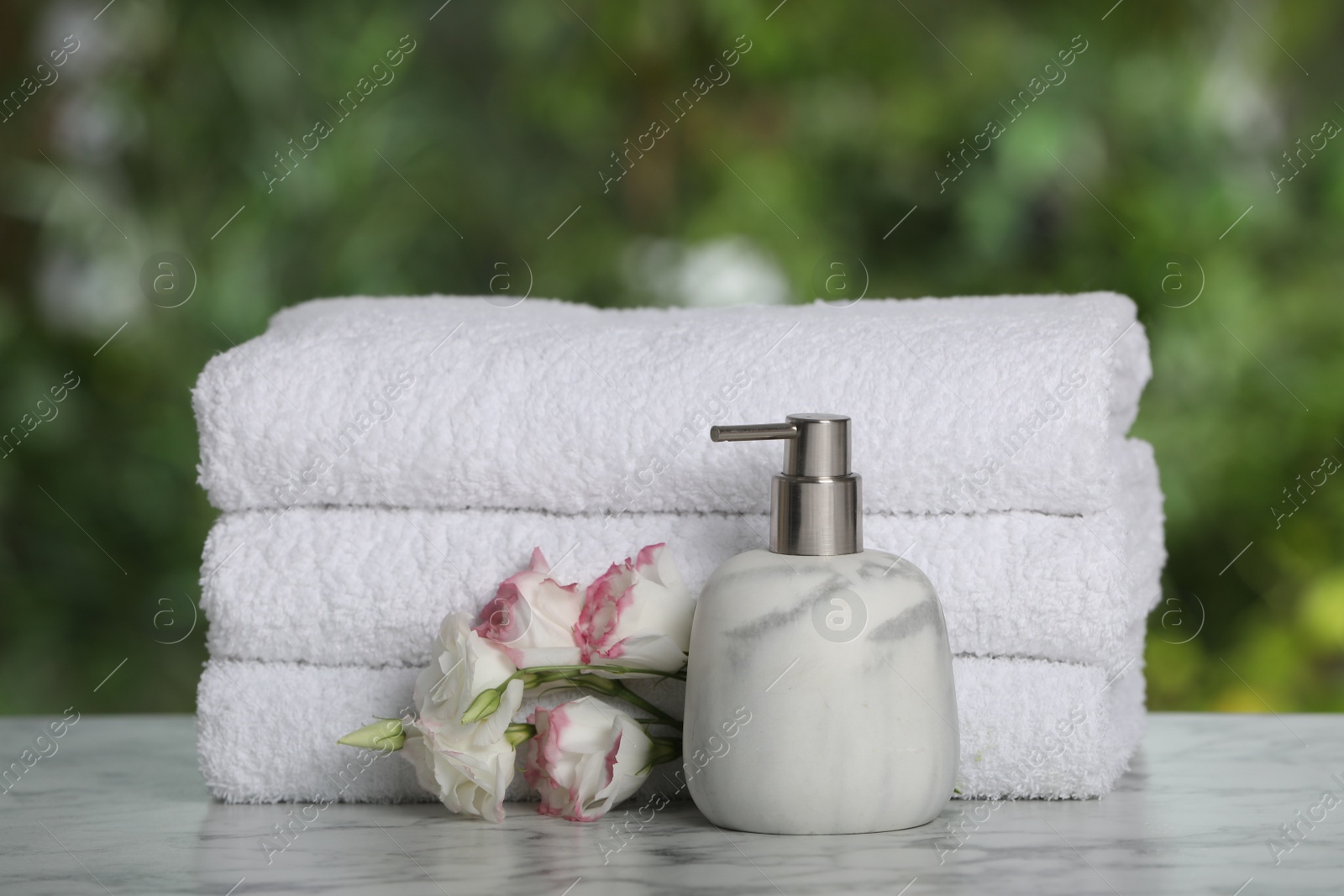 Photo of White soft towels, dispenser and flowers on marble table outdoors, closeup