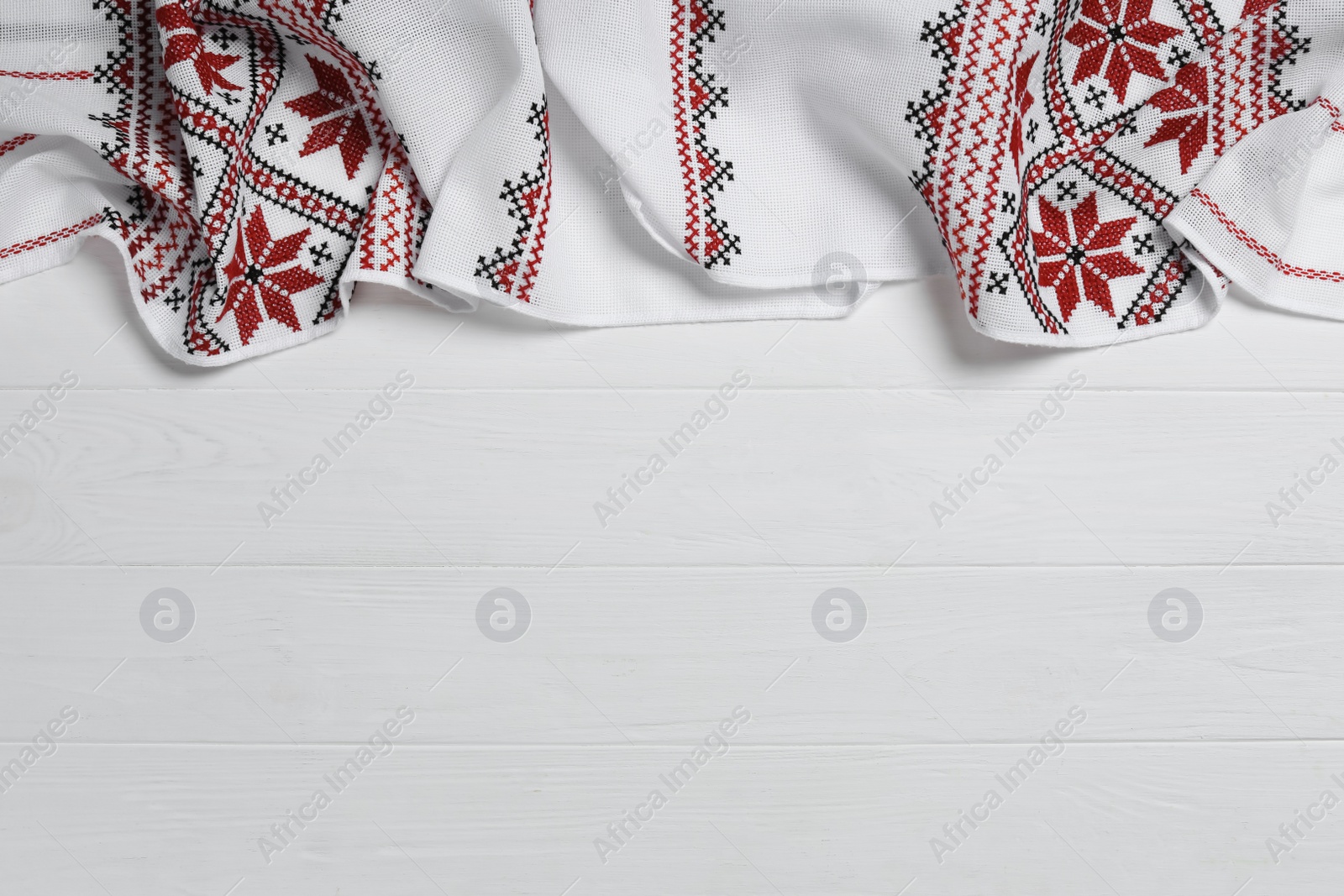 Photo of Beautiful rushnyk on white wooden table, top view with space for text. Ukrainian national embroidery