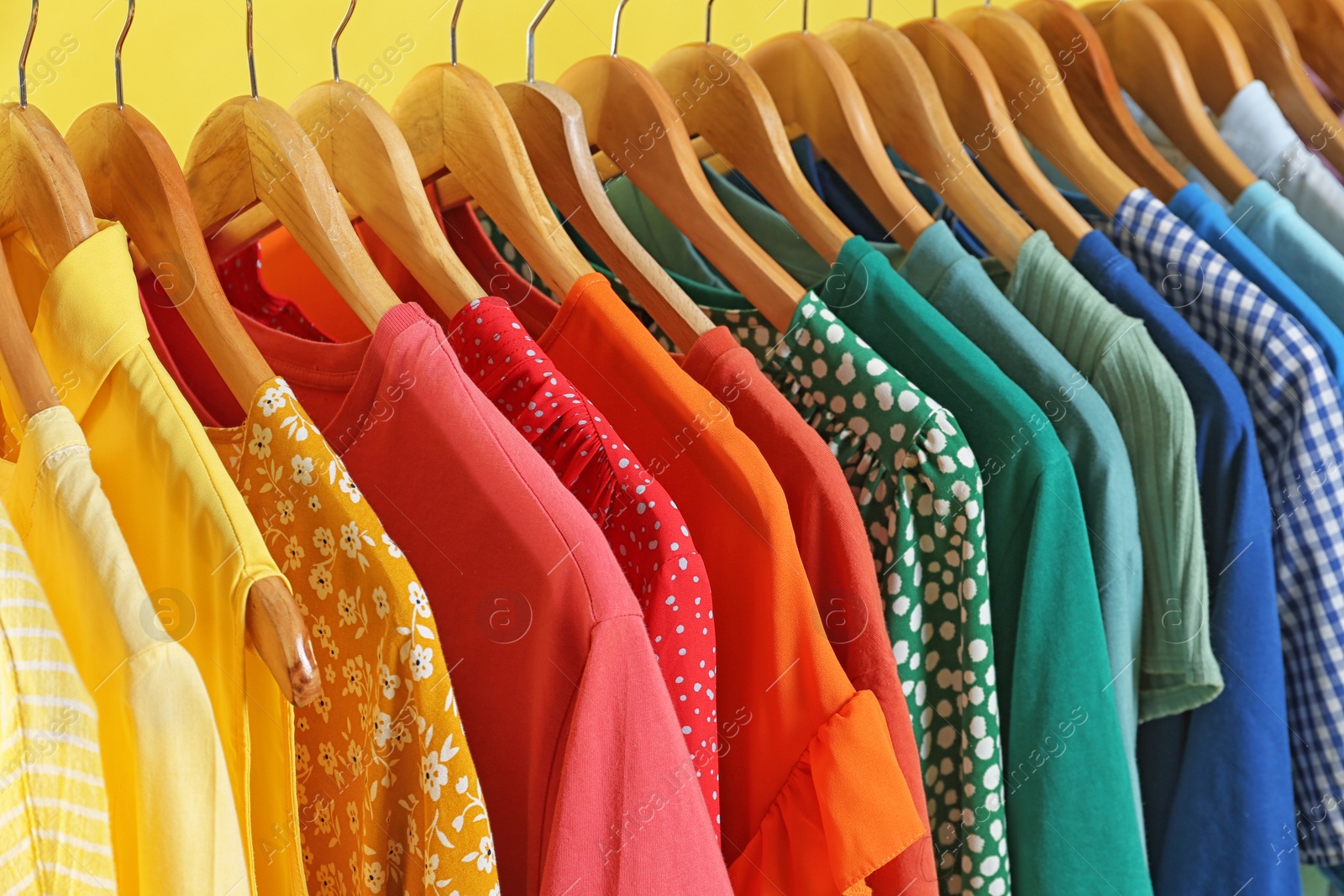 Photo of Bright clothes on hangers against yellow background, closeup. Rainbow colors