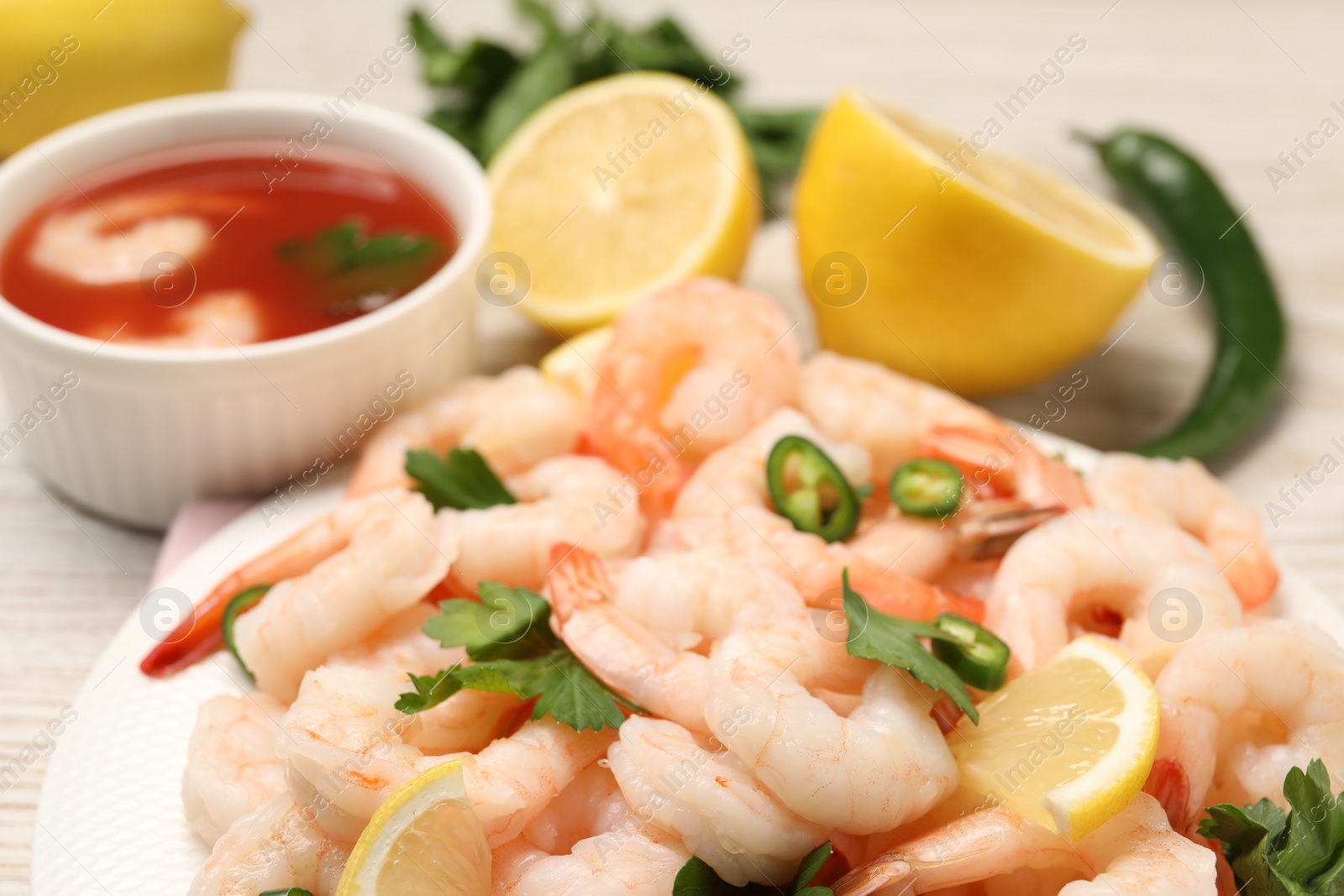 Photo of Tasty boiled shrimps with cocktail sauce, chili and parsley on table, closeup