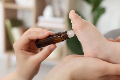 Photo of Mother applying essential oil from roller bottle onto her baby`s heel indoors, closeup