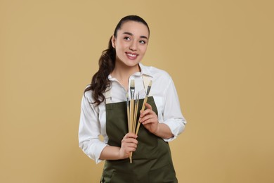 Photo of Woman with paintbrushes on beige background. Young artist