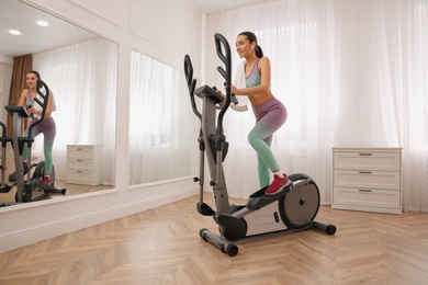 Photo of Woman with towel using modern elliptical machine at home