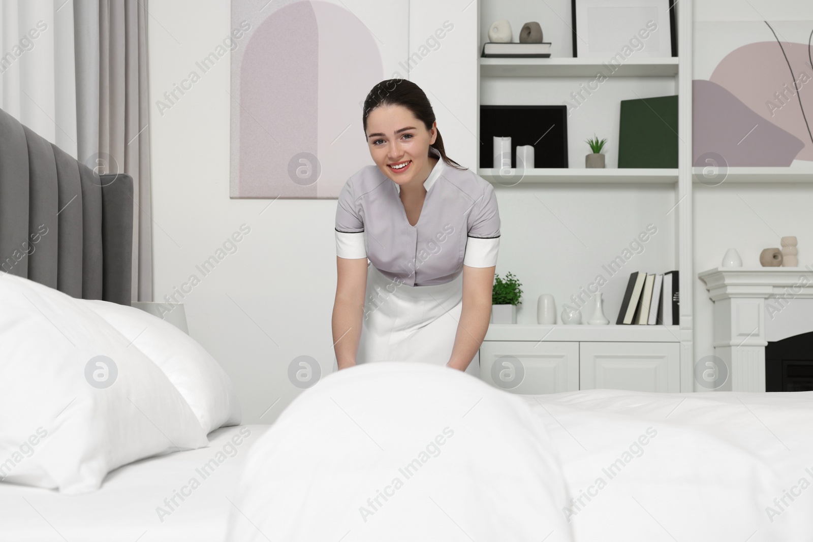 Photo of Young chambermaid making bed in hotel room