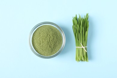 Wheat grass powder in glass bowl and fresh sprouts on light blue table, flat lay