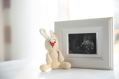 Photo of Ultrasound photo of baby and toy on table indoors, space for text