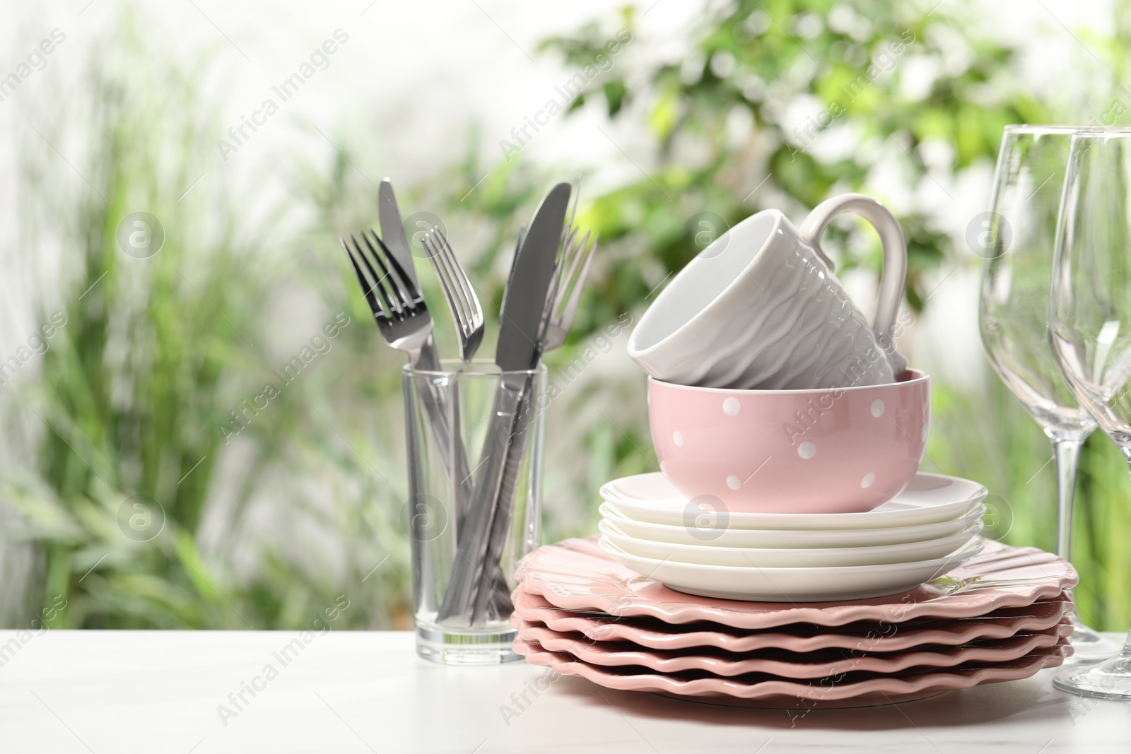 Photo of Beautiful ceramic dishware, glasses, cutlery and cup on white table outdoors, space for text
