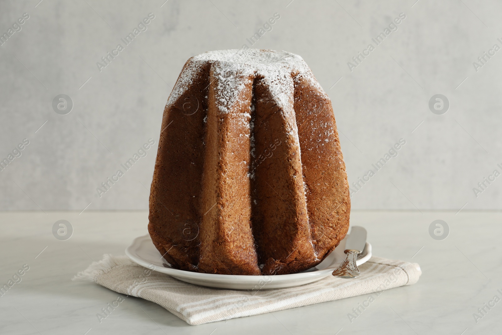 Photo of Delicious Pandoro cake decorated with powdered sugar on white table. Traditional Italian pastry