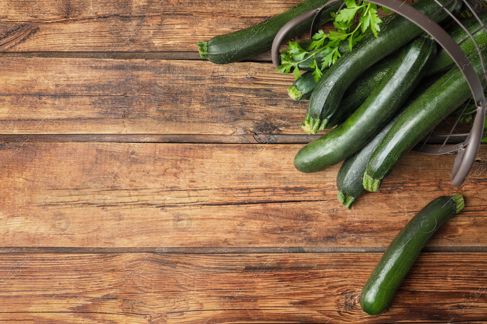 Photo of Basket with green zucchinis on wooden table, flat lay. Space for text