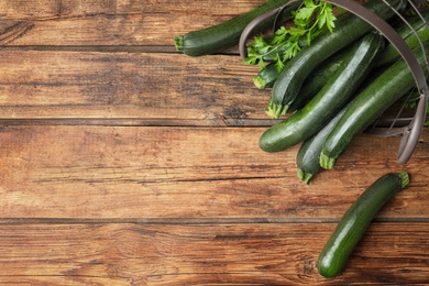 Basket with green zucchinis on wooden table, flat lay. Space for text