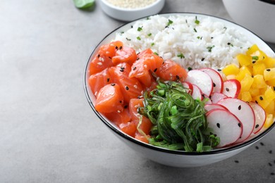 Delicious poke bowl with salmon and vegetables on light grey table, closeup. Space for text
