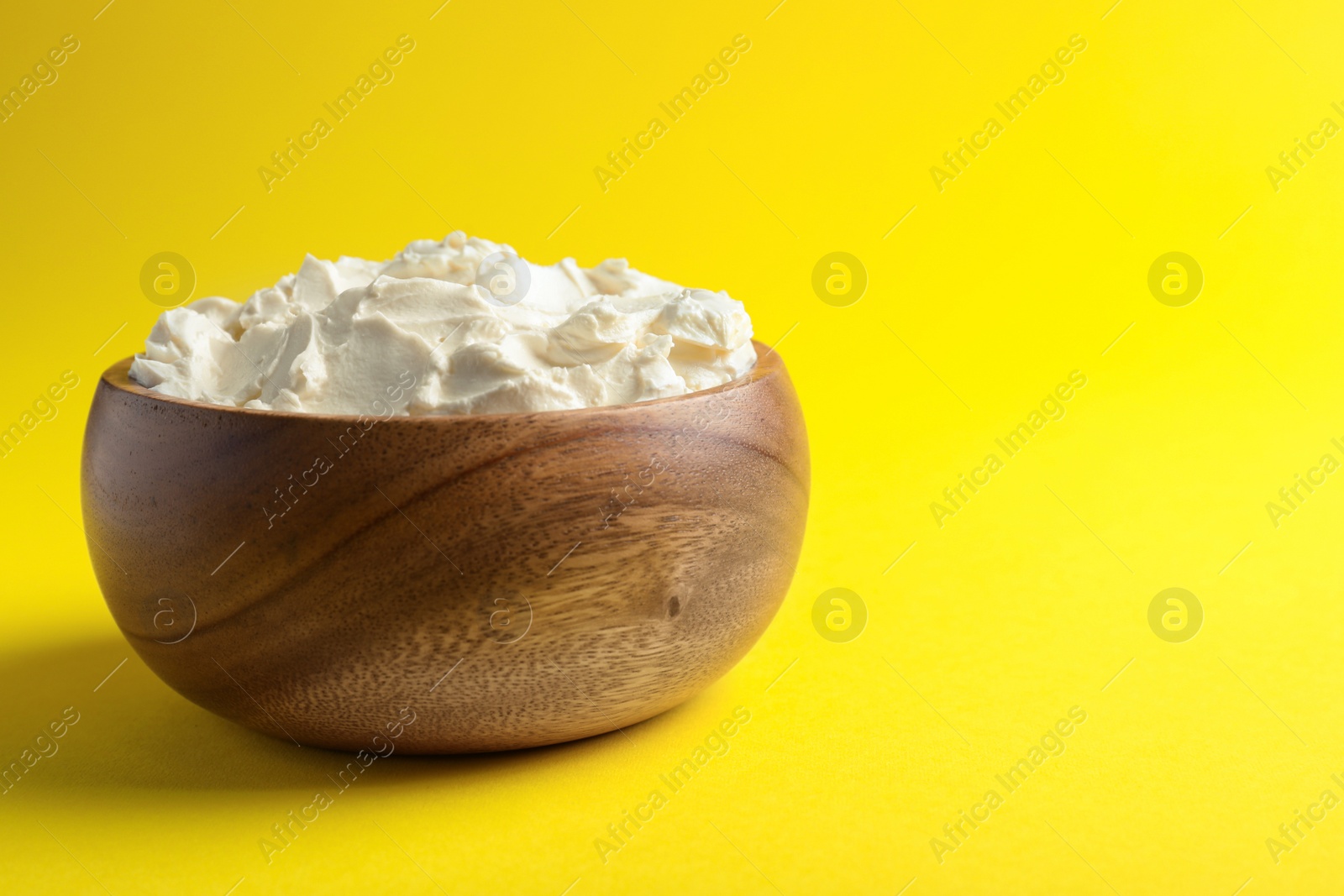 Photo of Bowl of tasty cream cheese on yellow background, space for text