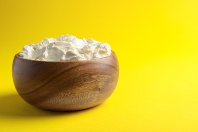 Photo of Bowl of tasty cream cheese on yellow background, space for text