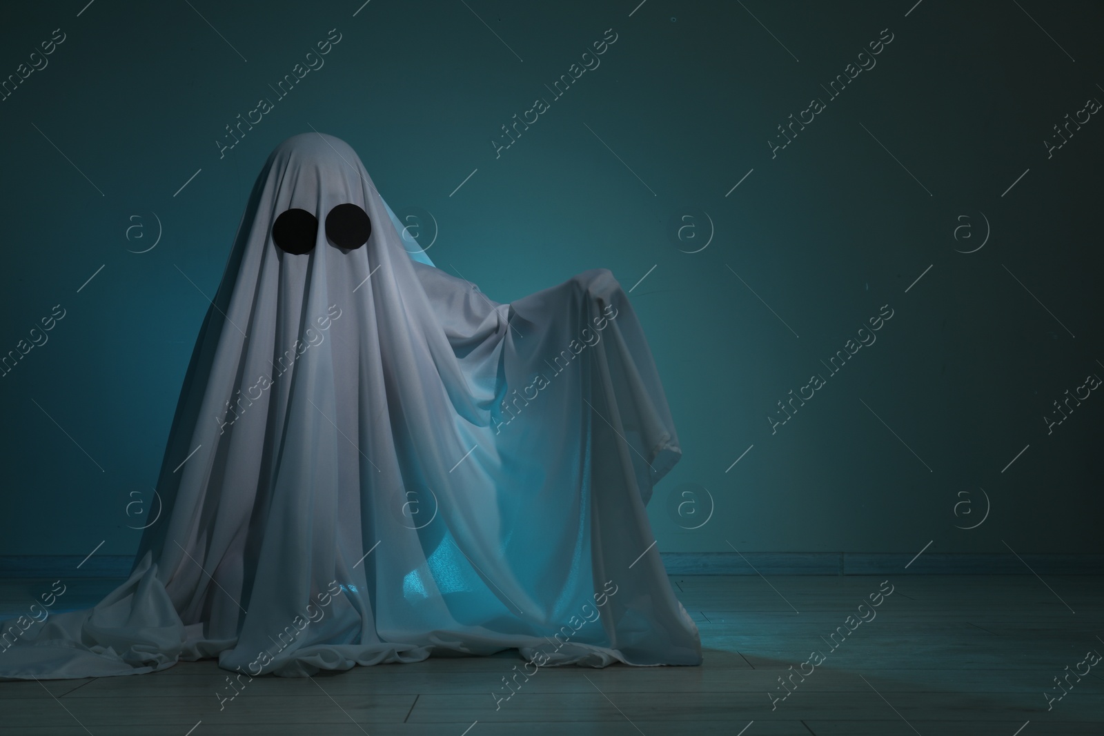 Photo of Creepy ghost. Woman covered with sheet on dark teal background, space for text