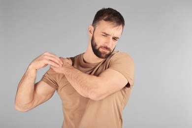 Young man suffering from pain in shoulder on light background