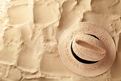 Photo of Stylish straw hat on sand, top view. Space for text