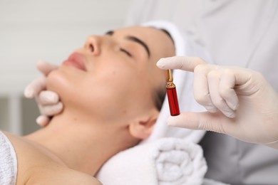 Professional cosmetologist holding skincare ampoule while working with client in clinic, closeup