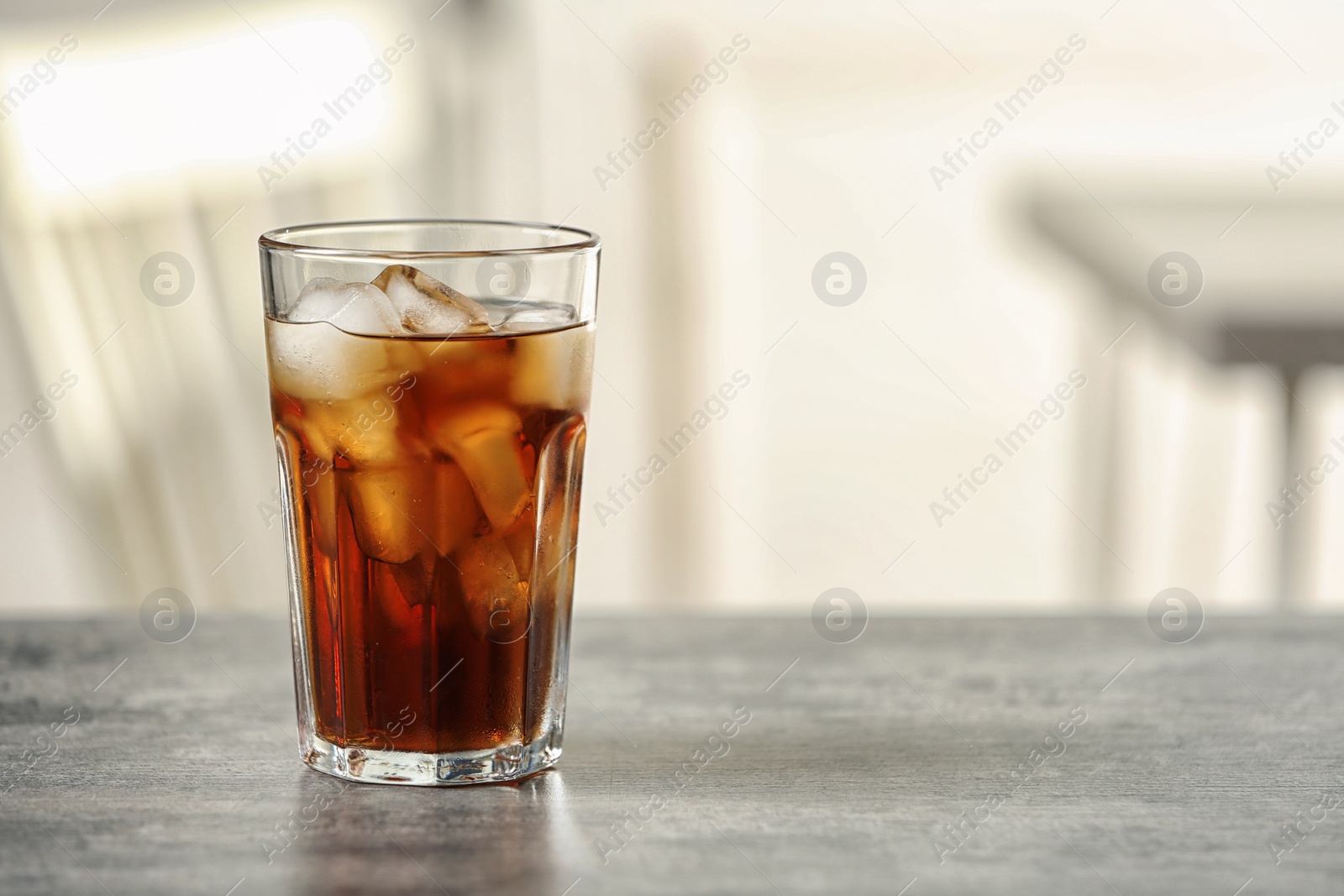 Photo of Glass of cola with ice on table against blurred background, space for text