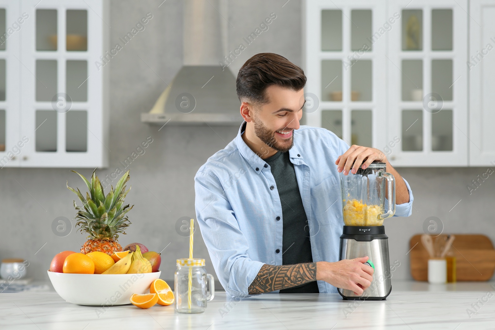 Photo of Handsome man preparing ingredients for tasty smoothie at white marble table in kitchen