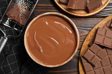 Photo of Tasty milk chocolate paste in bowl, pieces and grater on wooden table, flat lay