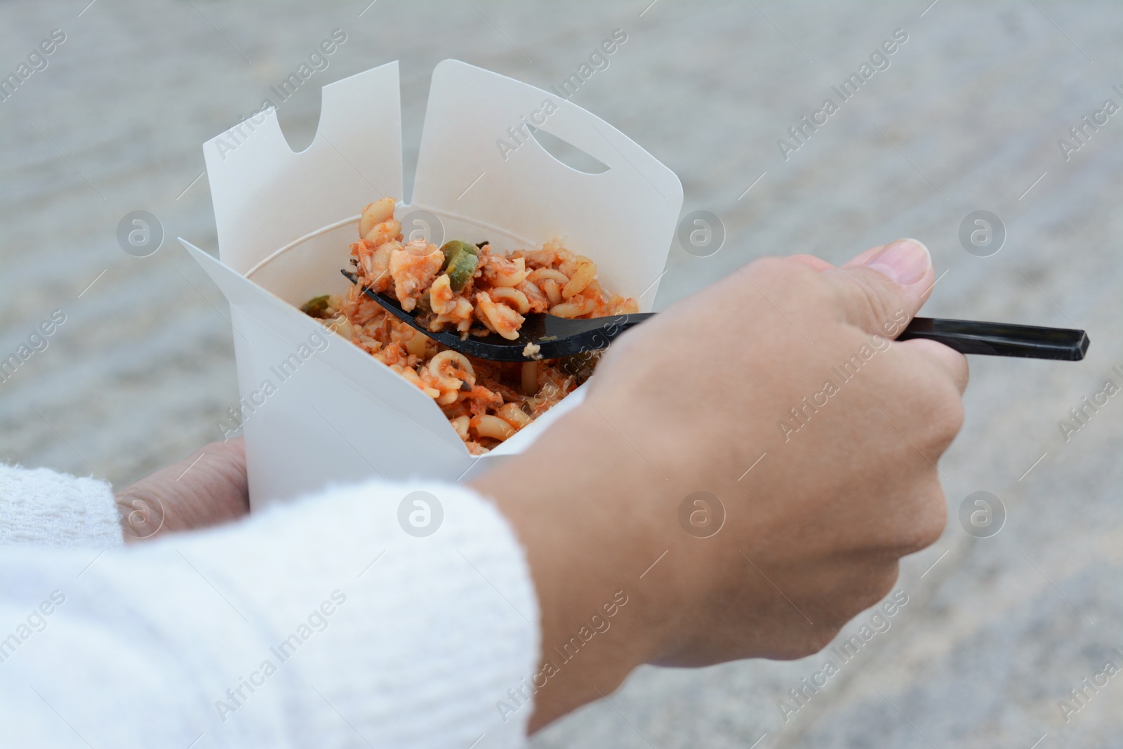 Photo of Woman eating takeaway noodles from paper box with fork outdoors, closeup. Street food