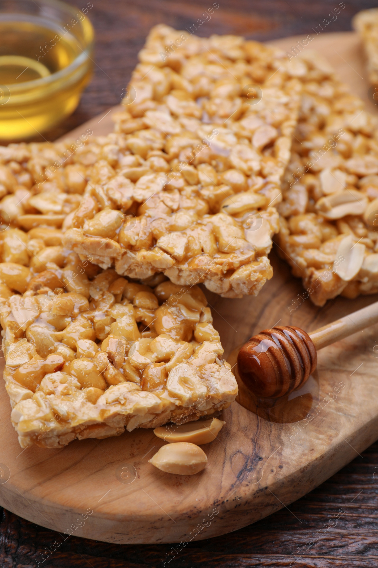 Photo of Delicious peanut bars (kozinaki) and dipper with honey on wooden table, closeup